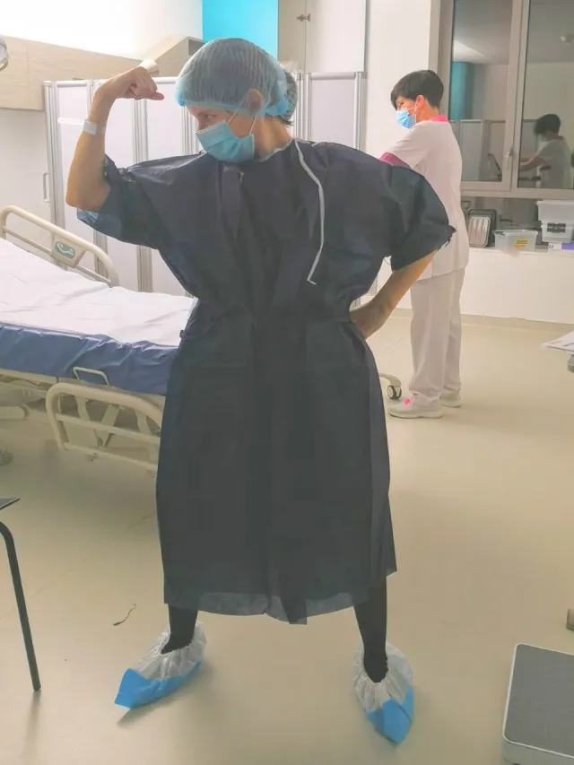 Solenn de la Croix, co-founder of JOJO, in a hospital gown, raising her arm as a sign of strength.